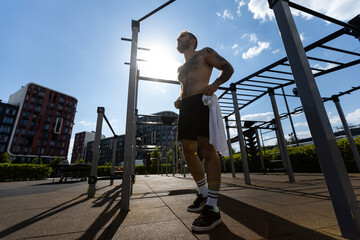 Muscular bodybuilder handsome man with naked torso trains triceps in a crossover cable exercise machine on the street