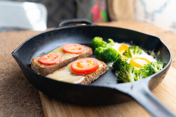 fried eggs with broccoli and whole grain toast with cheese and tomato in a cast iron skillet