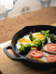 fried eggs with broccoli and whole grain toast with cheese and tomato in a cast iron skillet