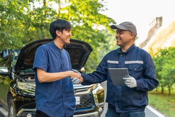 Handsome asian mechanic man shows the car report on a digital tablet to asian client at the roadside, A mechanic and a customer discussing repairs problems to his vehicle.