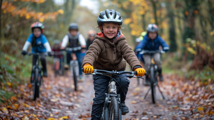 Fototapeta premium Young boy smiling and leading a group of children on a bike ride through a forest trail covered in autumn leaves.