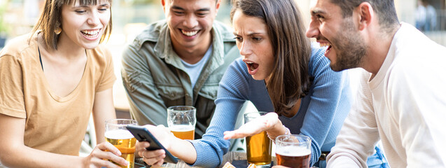 Group of multiethnic friends reacting to something on a smartphone at an outdoor café. They are enjoying drinks and showing a range of emotions.