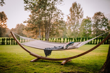 Blome, Latvia - September 11, 2023 - A hammock with pillows and a blanket on a green lawn, surrounded by trees and bushes, creating a peaceful outdoor relaxation spot. Copy space.