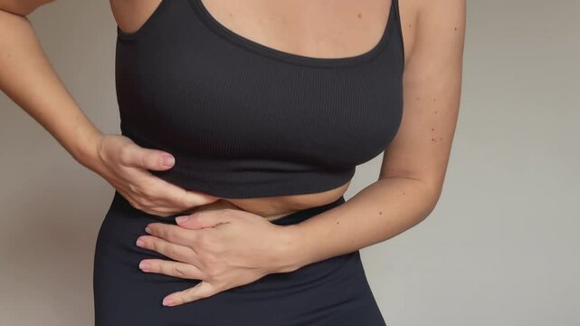 Young woman holding her side with her hands on beige background. Sore side under the right rib. Stomach pain, diseases of the gallbladder and liver, attack of cholecystitis, dyskinesia, gallstones