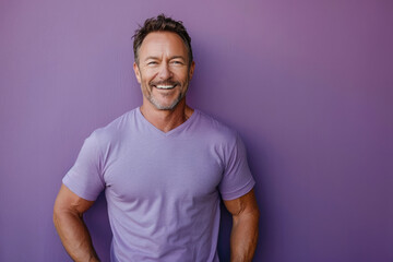 Obraz premium A happy mature man with hands on hips, smiling broadly, dressed in a purple T-shirt, standing against a plain purple backdrop