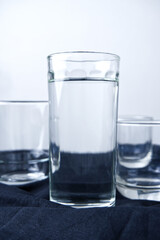 Glass of water with white background. Drinking, clean water, healthy drink, liquid, and tableware concepts. Vertical image of pure and room temperature of water glasses on black fabric.