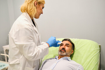 Fototapeta premium A man is getting Botox or filler for forehead wrinkles by a aesthetic doctor in a clinic.
