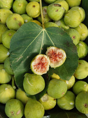 Abundance of figs. Vertical flat lay of ripe green figs with a fig leaf and a halved fig on it exposing its red inner juicy red flesh. Sardinia, Italy.