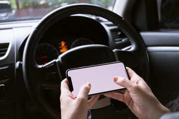 Woman sitting in a car and holding a smartphone with blank screen.