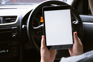 Woman sitting in a car and holding a tablet with blank screen.
