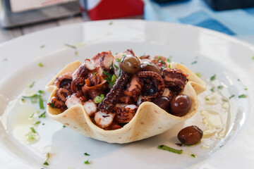 Tasty grilled octopus with potato and olive on a table in restaurant