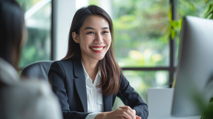 Smiling Asian businessman sitting and talking with customers in the office. with a white desktop computer on a table, giving advice or consulting on business or financial problems of customers