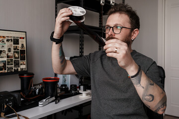 A modern photographer holds film negatives up to the light, inspecting them in a workspace filled with photography equipment.
