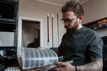 Hipster photographer focused on examining film negatives, surrounded by photo equipment in a cozy studio environment.