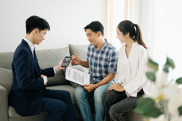 Asian man Real estate broker agent showing a house detail in her file to the young Asian couple lover looking and interest to buy it.