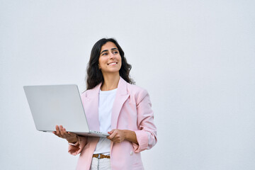Dreaming young middle eastern Israel businesswoman using laptop pc online application for work isolated on white wall. Indian, arabic woman in business suit holding computer, looking aside. Copy space