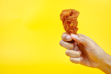 Female hand holding fried chicken on yellow background.