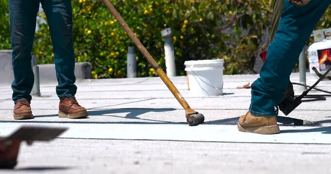 Roofer applying granulated APP Torch Down and Using a Roller