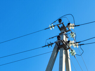 Concrete pillars with electrical wires, coils of cables, connecting wires and insulators. Electricity transmission, power supply. View from below, against clear blue sky background, without clouds.