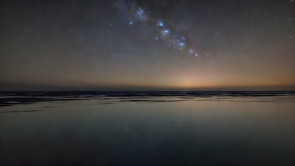 The stars reflecting off the calm surface of the ocean, with the horizon line barely visible.