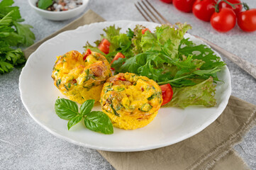 Egg muffins or egg bites with bacon, cheese, vegetables and herbs on a white plate on a concrete background. Healthy breakfast.