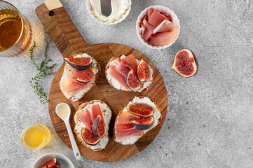 Bruschetta or toast with goat cheese spread, prosciutto, figs and honey on a board.