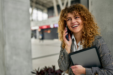 Amidst the railway station, a cheerful young woman in casual clothes walks, talks on the phone, and...