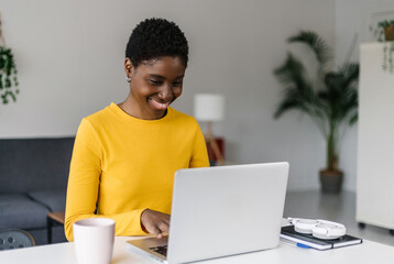 Happy young african woman working on laptop at home. Millennial black student studying online with computer. Education or business concept.