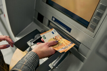Zooming in on the moment, the woman confidently retrieves crisp bills from the ATM, completing a seamless and secure financial transaction.