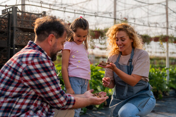 Mother showing a bulb to her daughter, with the father participating, teaching about plant biology in their greenhouse.