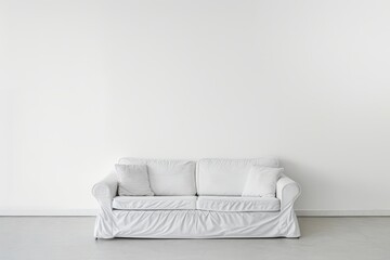 A white sofa with two pillows sits in front of a blank white wall