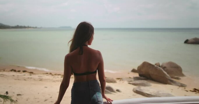 Woman relax standing on a balcony of a resort in Thailand, gazes out at the peaceful ocean. Tropic nature coastline landscape in background. Female tourist on summer vacation. Lifestyle holiday