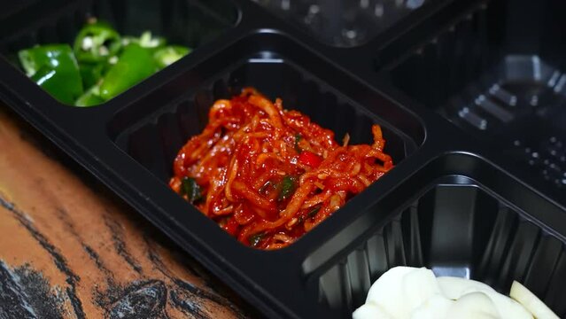 Hands carefully arranging a variety of vibrant vegetables into black meal prep containers for healthy eating.