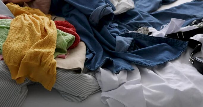 Bed with a Pile of Clothes. capturing the relatable moment of not knowing what clothes to choose. messy bed with many products on it. Consumer culture of buying too many. coming home after shopping.