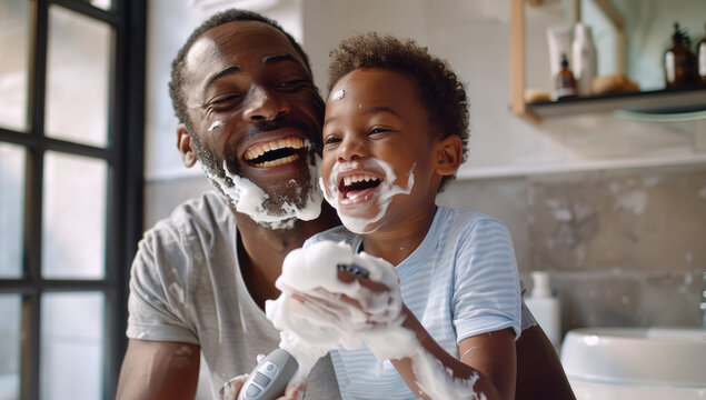 A father and son laugh as they dress up in the bathroom, covered with white facial cream on their faces and around their necks, sharing an adventure playing together using razor blades