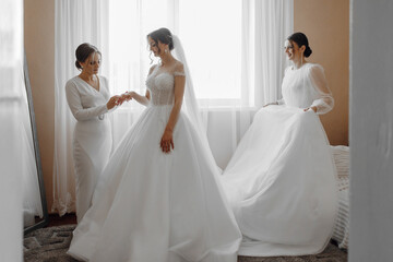 Naklejka premium Three women are getting ready for a wedding. One of them is wearing a white dress and the other two are wearing white dresses. The bride is getting ready with her mother and sister