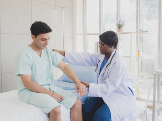 Obraz premium Portrait patient caucasian man with woman nurse carer physical therapist African-American two people sitting talk helping support give advice and holding hand arm inside hospital indoor room service.