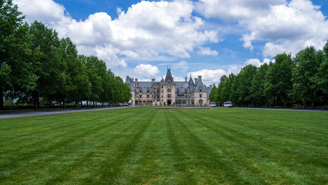 Wide-angle view of the Biltmore Estate with its grand architecture, expansive lawn, and surrounding trees under a partly cloudy sky.
