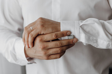A man is getting ready to dress up in a white shirt and is adjusting his cuff. Concept of preparation and attention to detail, as the man carefully straightens his cuff