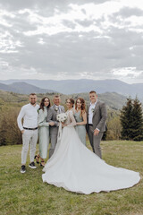 A bride and groom are standing in front of a group of family members. The bride is wearing a white dress and the groom is wearing a suit