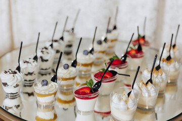 A table full of desserts with a variety of flavors and colors. The desserts are served in small plastic cups with spoons. The table is set up for a party or gathering