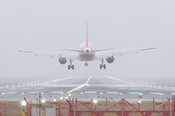 Rear view of a commercial airplane about to land on a foggy day.