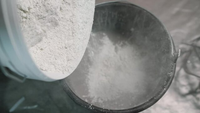 Adding hardener to a bucket of plaster. The white solution is poured into a bucket.