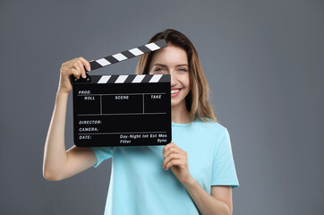 Making movie. Smiling woman with clapperboard on grey background