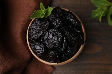 Tasty dried plums (prunes) and mint leaves in bowl on wooden table, flat lay