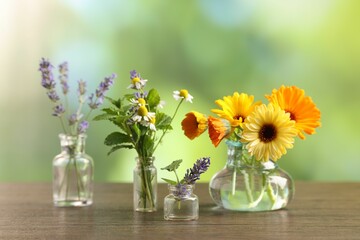 Different flowers in glass bottles on wooden table