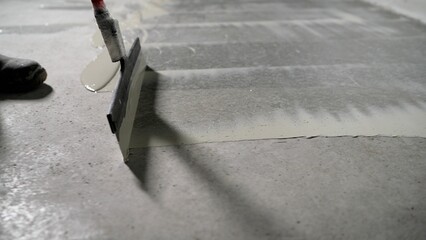 Installing an epoxy floor over existing concrete. Smoothing the primer over the concrete floor with a spatula. Applying construction primer to the floor using a spatula.