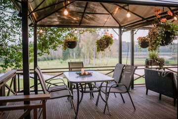 Blome, Latvia - September 11, 2023 - A cozy outdoor patio with hanging plants, string lights, and a table set with a candle, offering a serene view of the surrounding greenery.