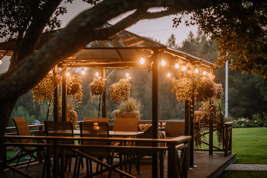 Blome, Latvia - September 11, 2023 - A cozy outdoor gazebo with hanging plants and string lights at dusk, surrounded by greenery, creating a warm and inviting atmosphere