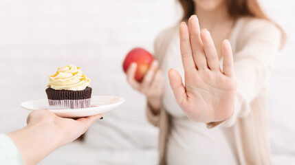 Dieting pregnancy. Pregnant woman refusing her favorite junk food such as croissant and choosing...